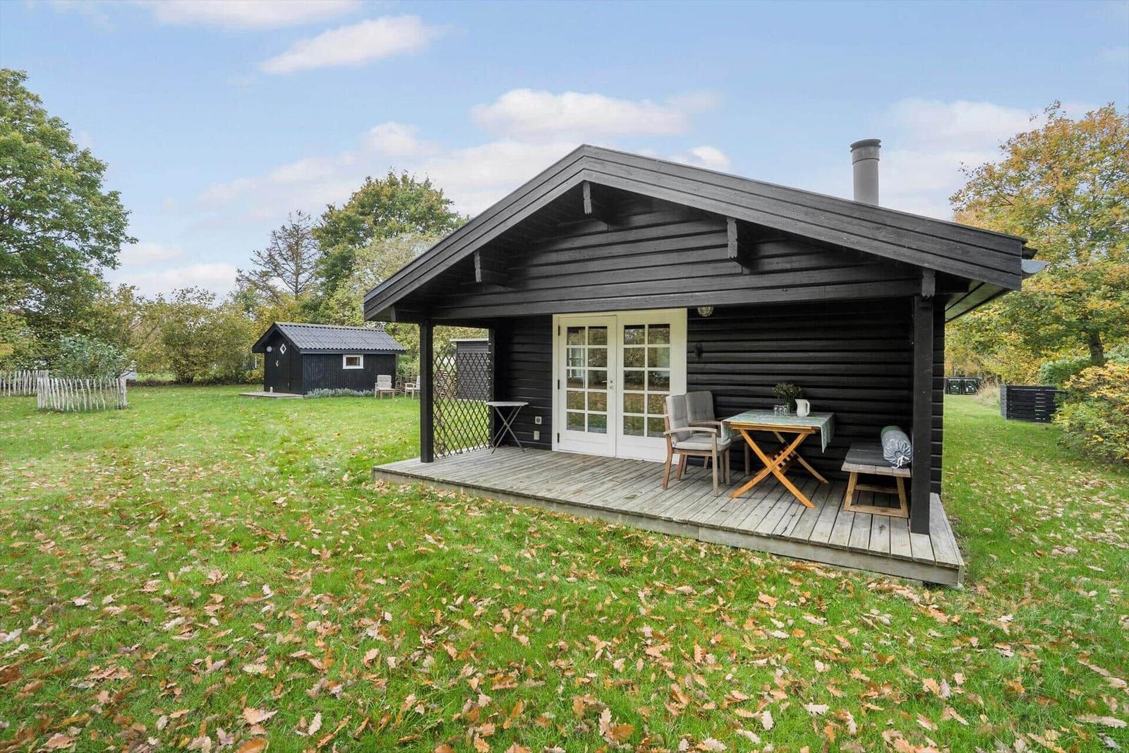 Schwarzes Holzhaus mit Garten, Sitzgelegenheiten und Bäumen im Hintergrund.