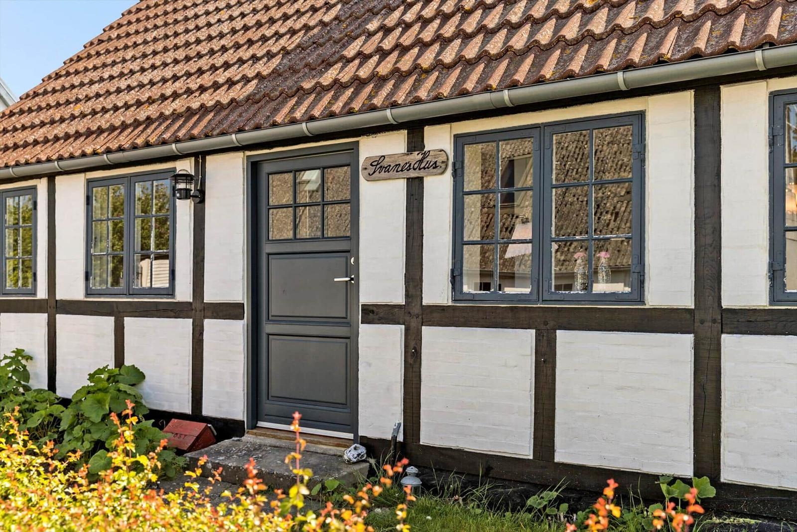 Haus mit rotem Ziegeldach, weißer Fassade und schwarzem Holzrahmen, umgeben von Grünflächen.