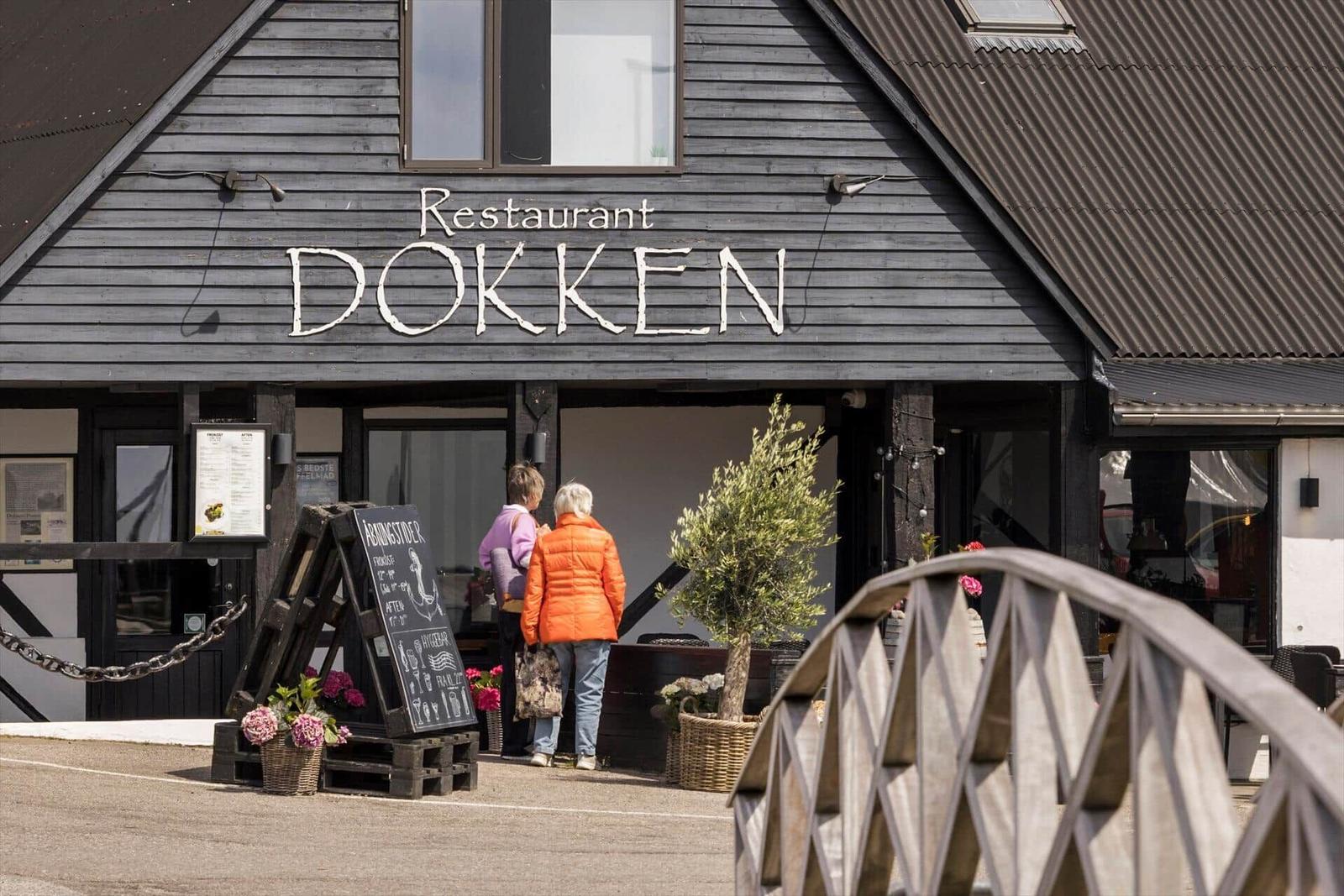 Weiße Kapelle mit rotem Dach, Fahrräder und Kinderwagen vor einem See.