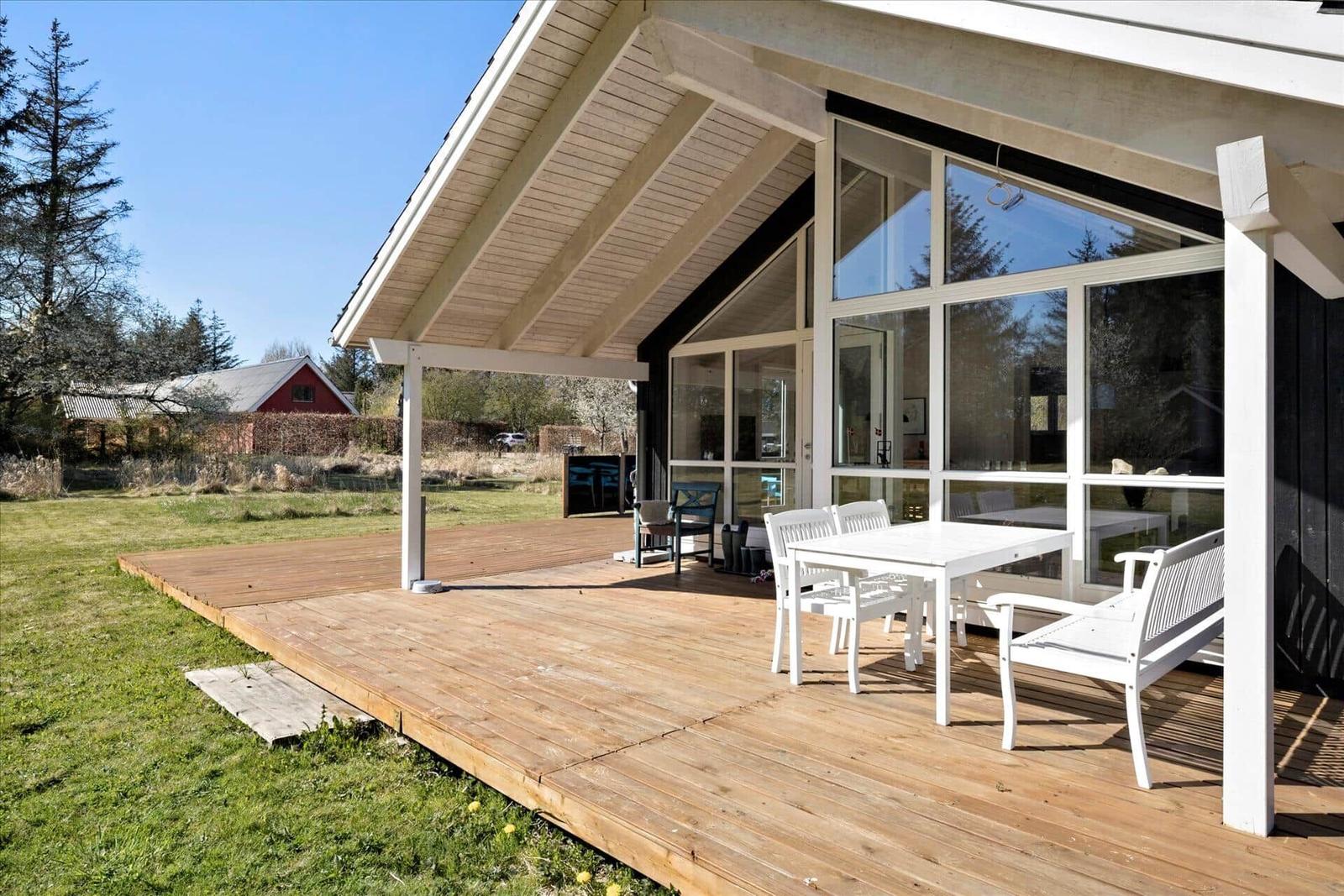 Schwarze Holzhütte mit Terrasse, umgeben von Gras und Bäumen.
