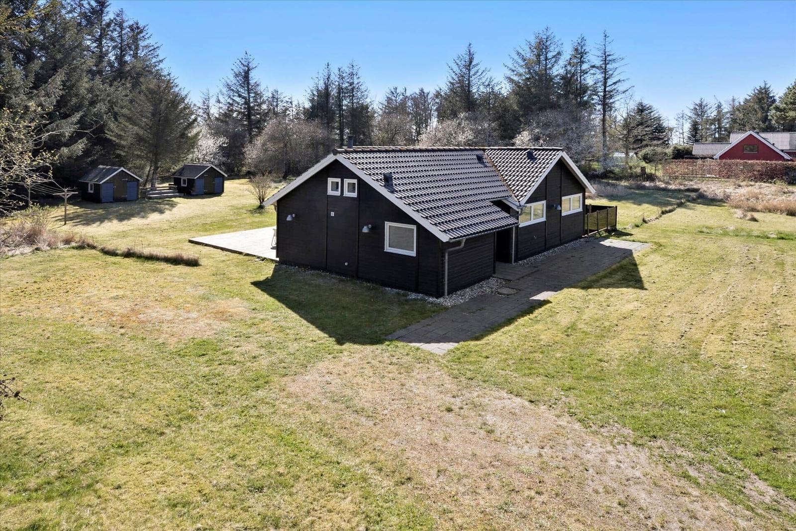 Moderne Hütte mit Holzterrasse und Garten. Umgeben von Bäumen und offenem Feld.