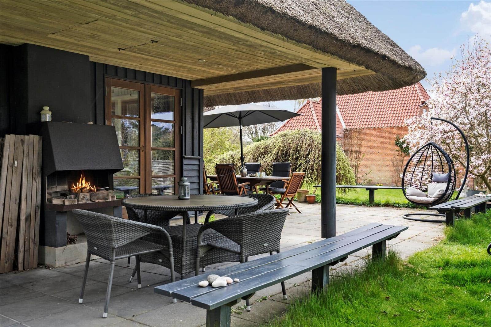Haus mit Strohdach und Garten. Terrasse mit Tisch und Stühlen.