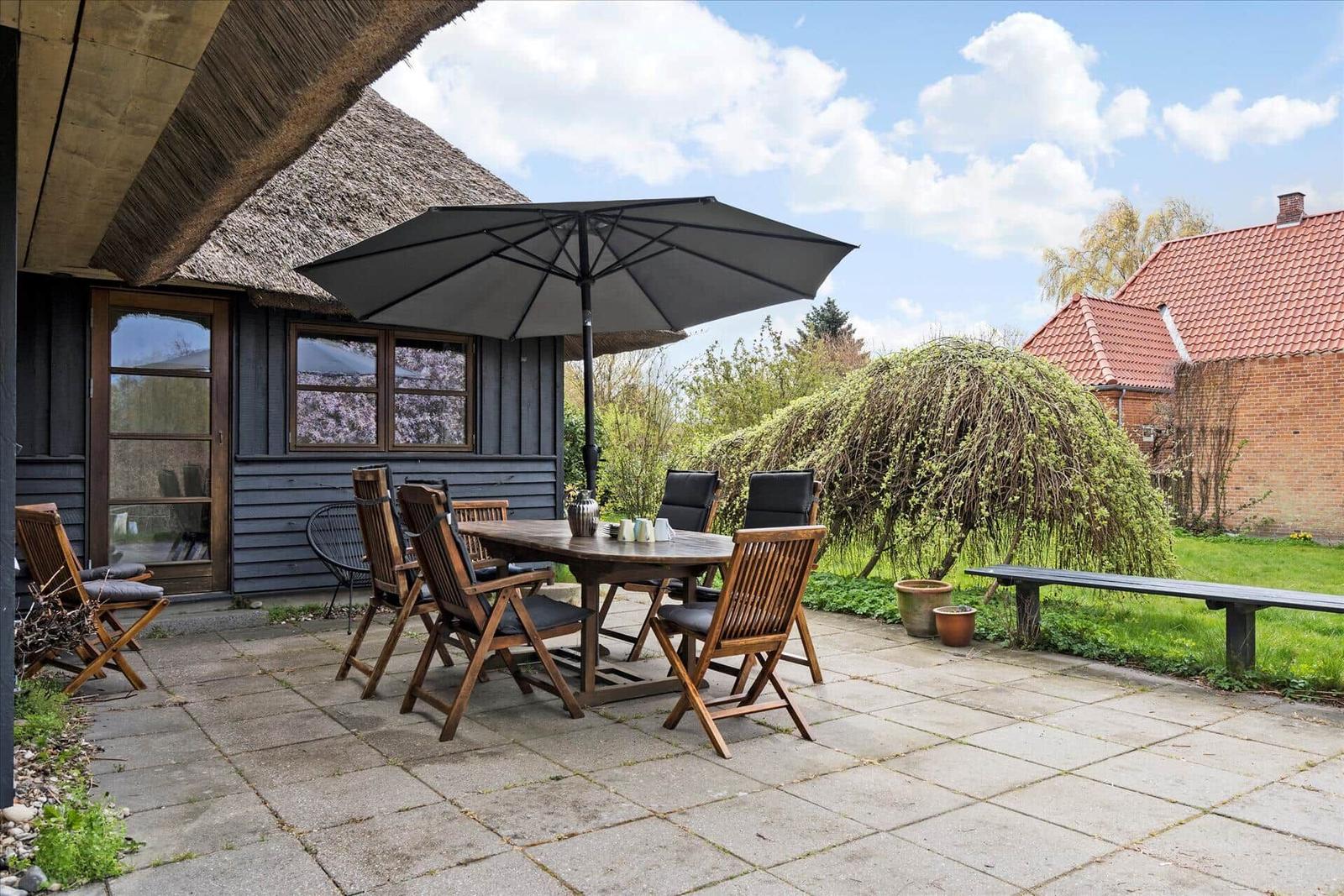 Haus mit strohgedecktem Dach und großem Gartenbereich mit Sitzgelegenheiten.