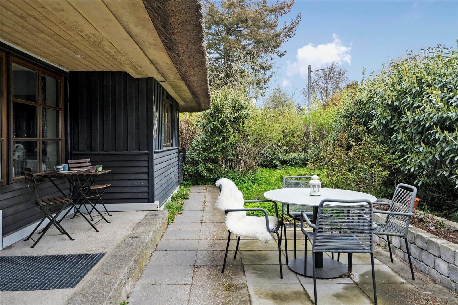 Außenbereich mit Tisch und Stühlen neben einem Haus mit Schilf.