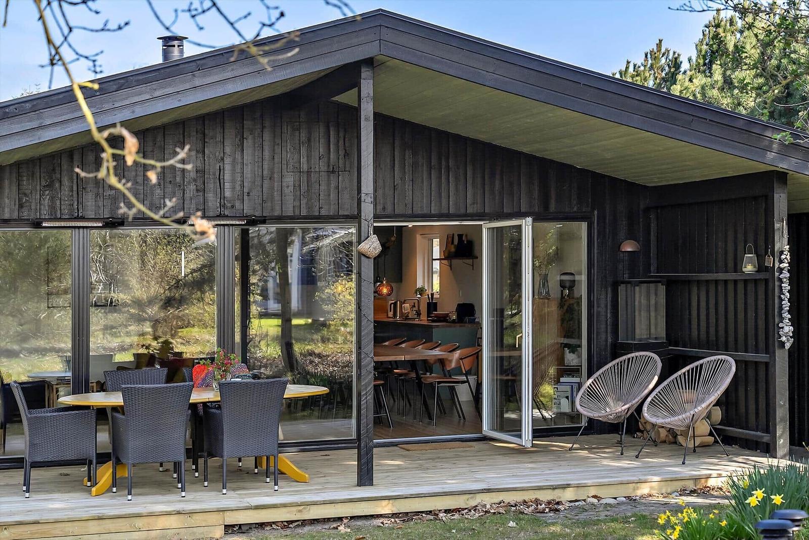 Schwarzes Holzhaus mit Terrasse und Sonnensegel auf grünem Rasen.