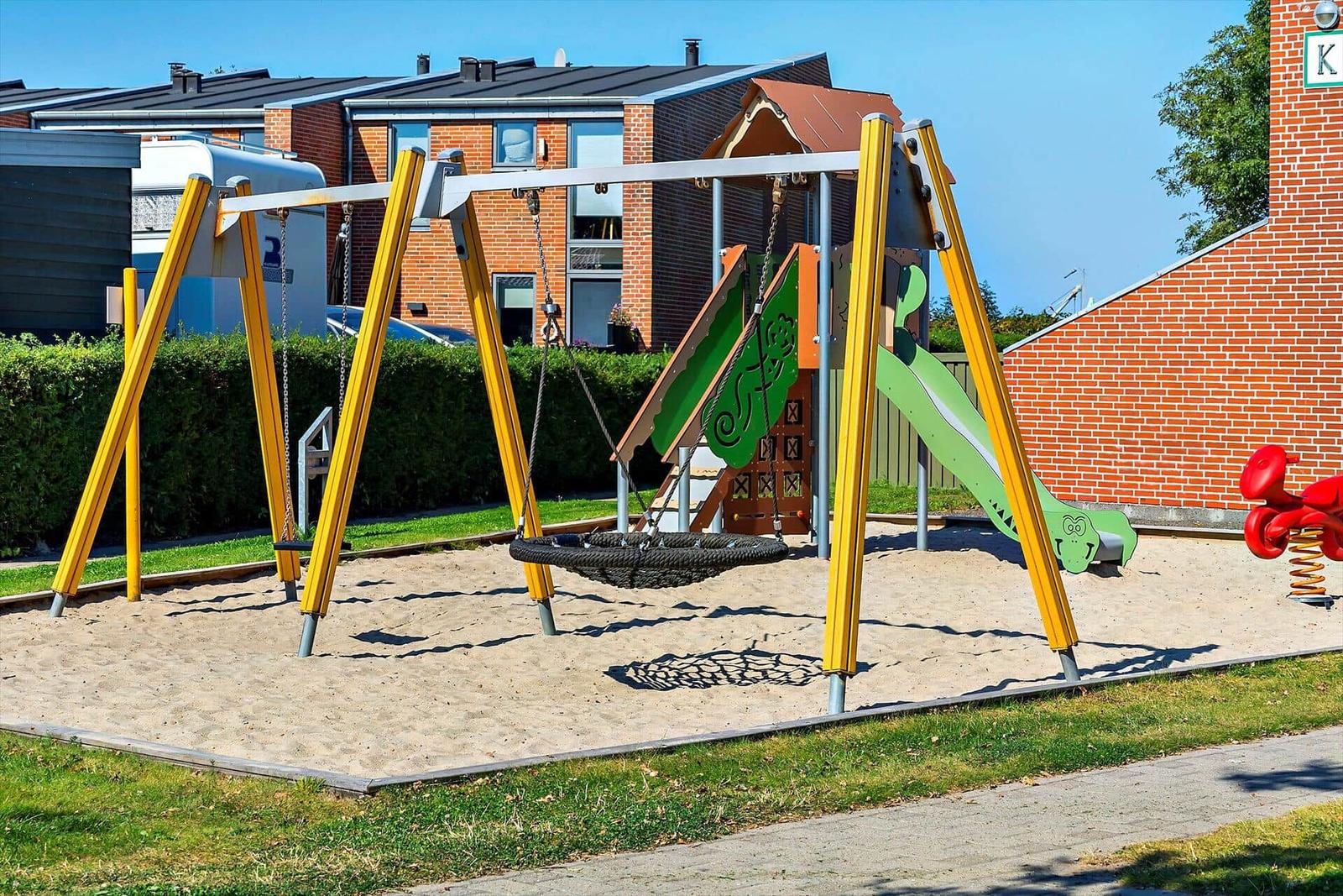 Kinderspielplatz mit Sandkasten, Schaukel und Tisch im Garten vor Wohnhäusern.