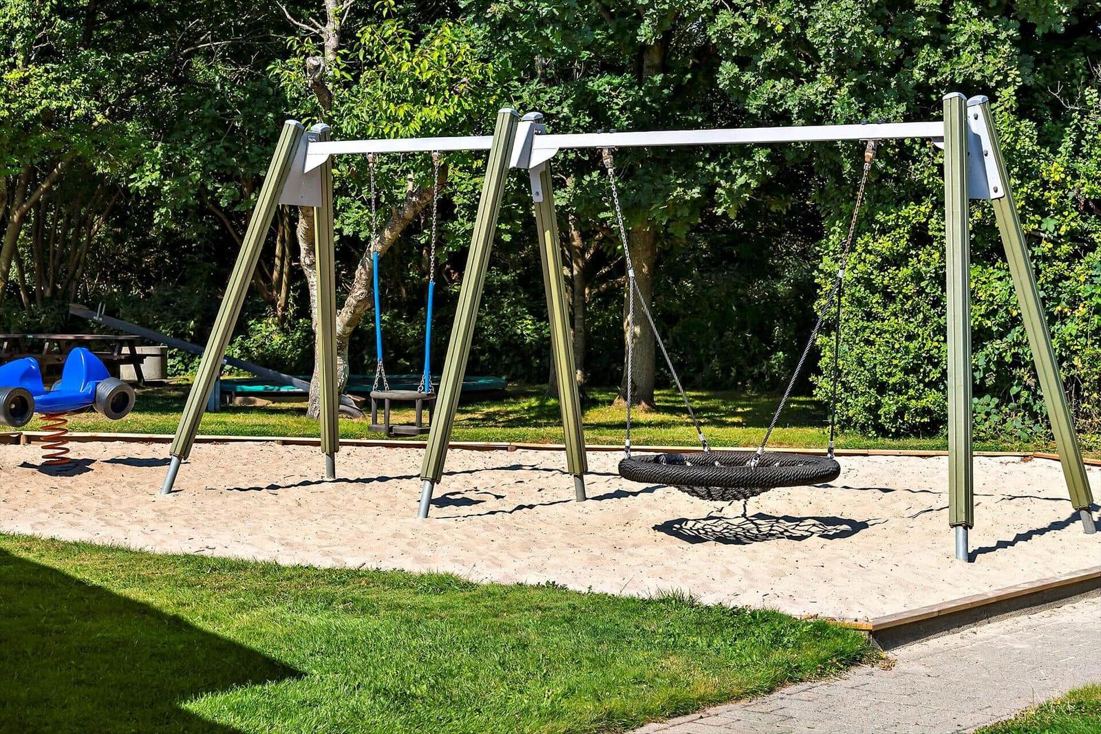 Kinderspielplatz mit Schaukel, Rutsche und Sandkasten vor Wohnhäusern.