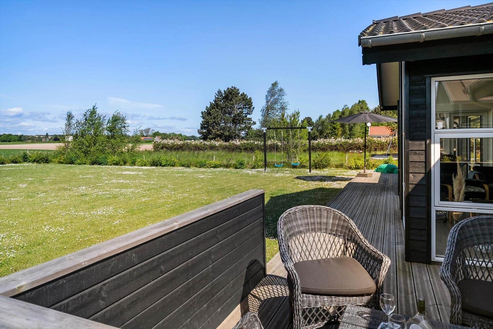 Terrasse mit Sitzgelegenheit und Blick auf grünes Feld und kleines Haus.