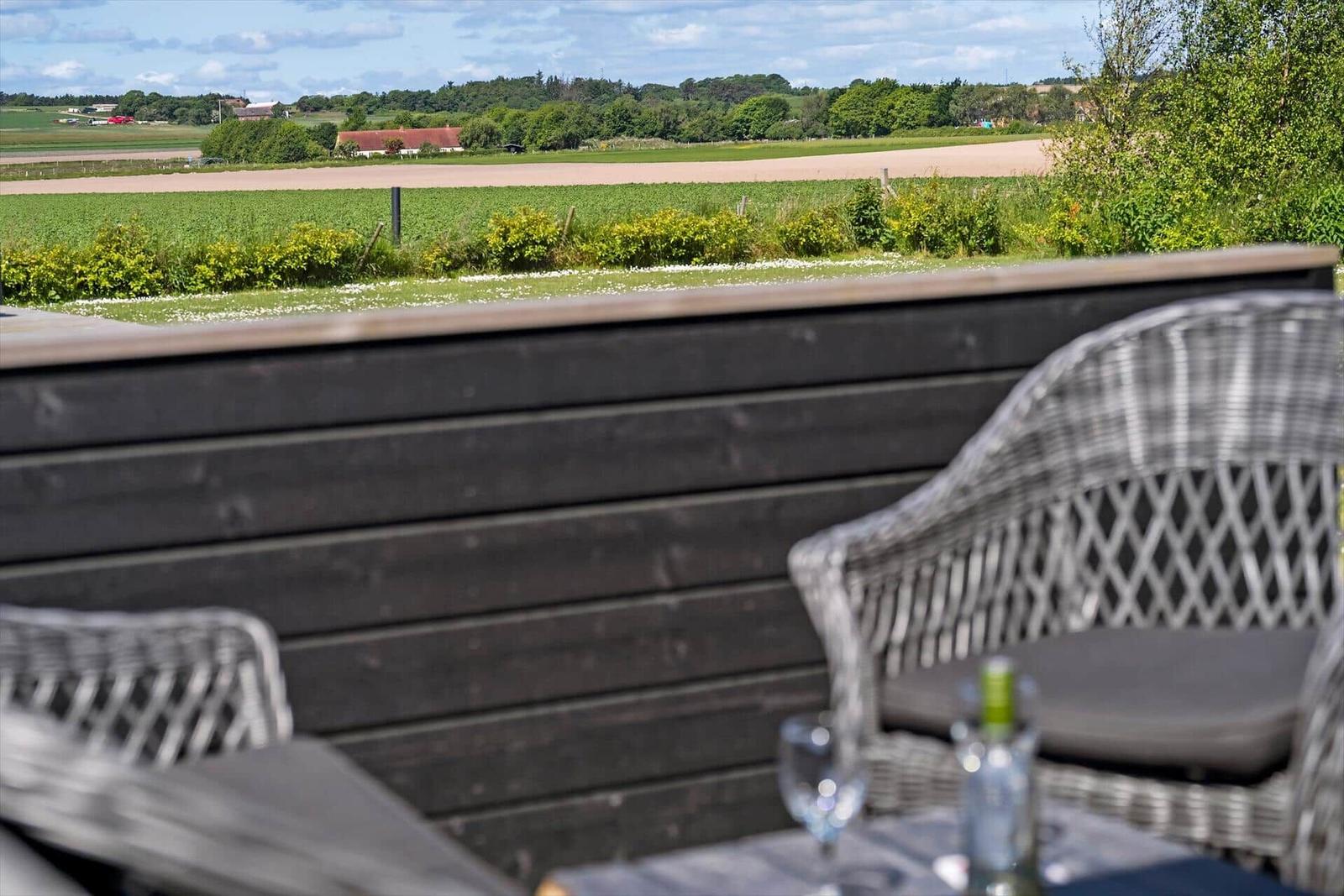 Grasland mit Holztisch und Strandkorb, Blick auf das Meer und eine Insel.
