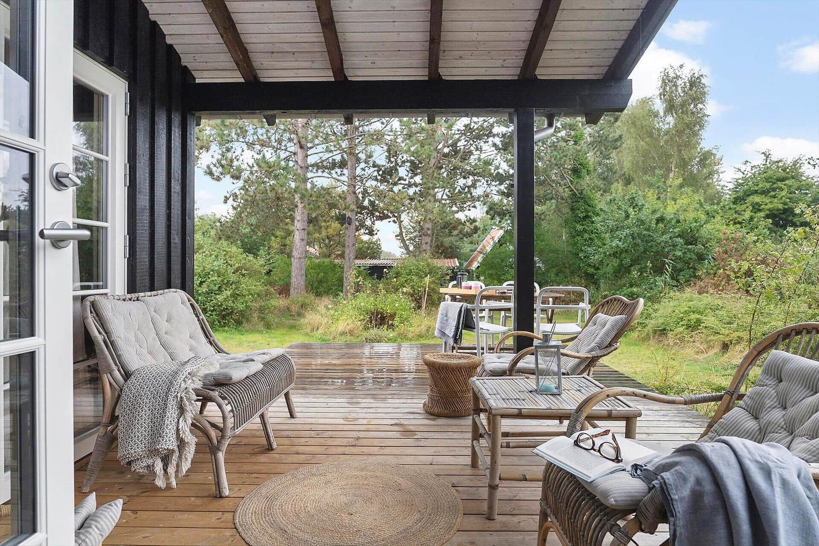 Black wooden house with white window and garden furniture in green.