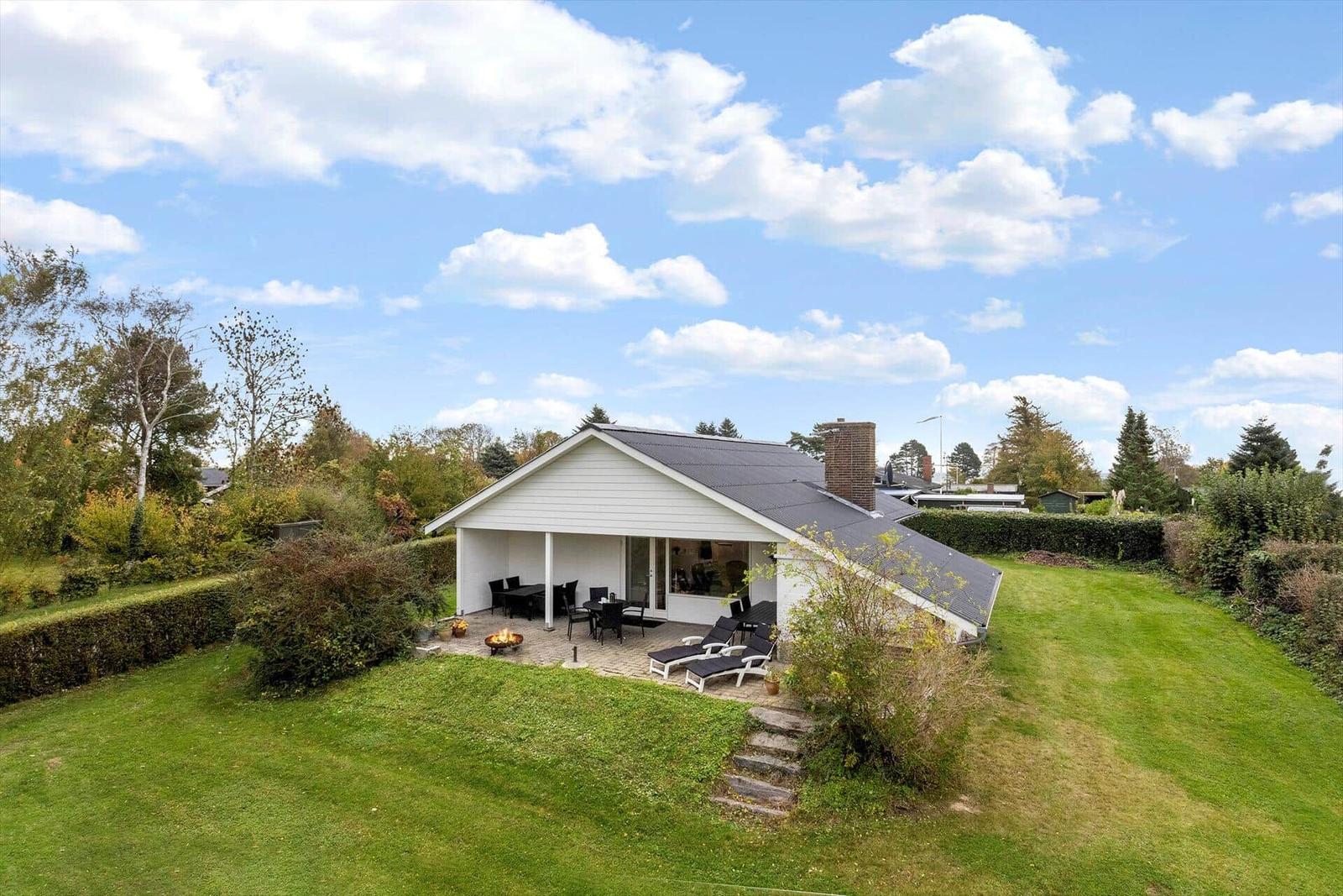 House with terrace, garden, and autumn leaves under blue sky.