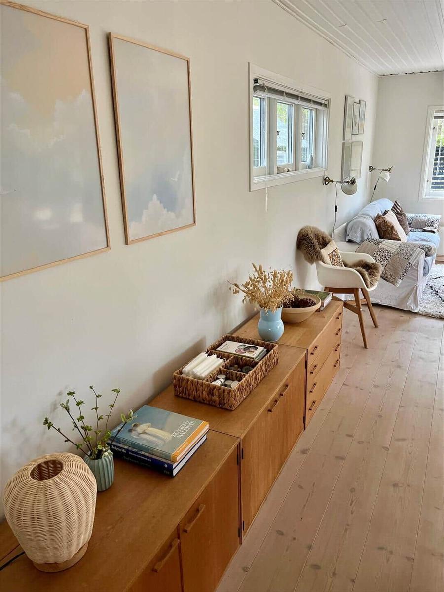 Living room with sofa, cushions, table, and windows. Pictures hang on the wall.