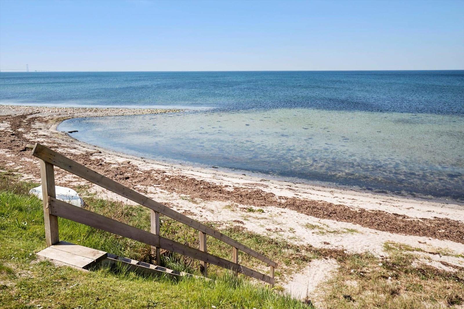Holzsteg führt zu Strand und Meer. Gras und Blumen am Hang.