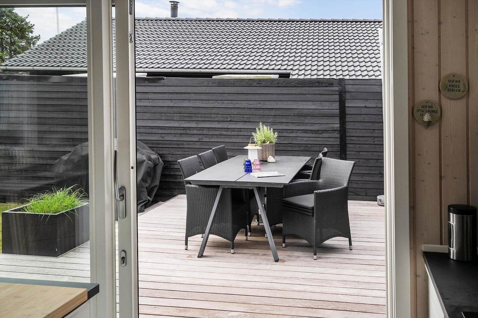 Moderne Holzhütte mit Garten und Terrasse. Eingangstür und Fenster mit weißen Rahmen.