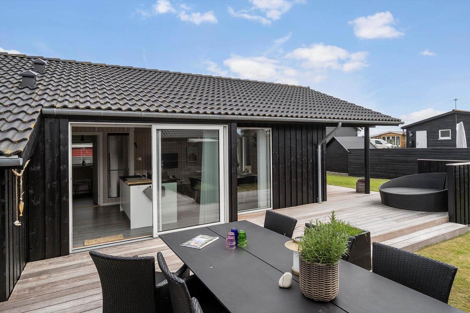 Moderne Holzhütte mit Terrasse und Garten. Glasfront öffnet sich zum Innenraum.