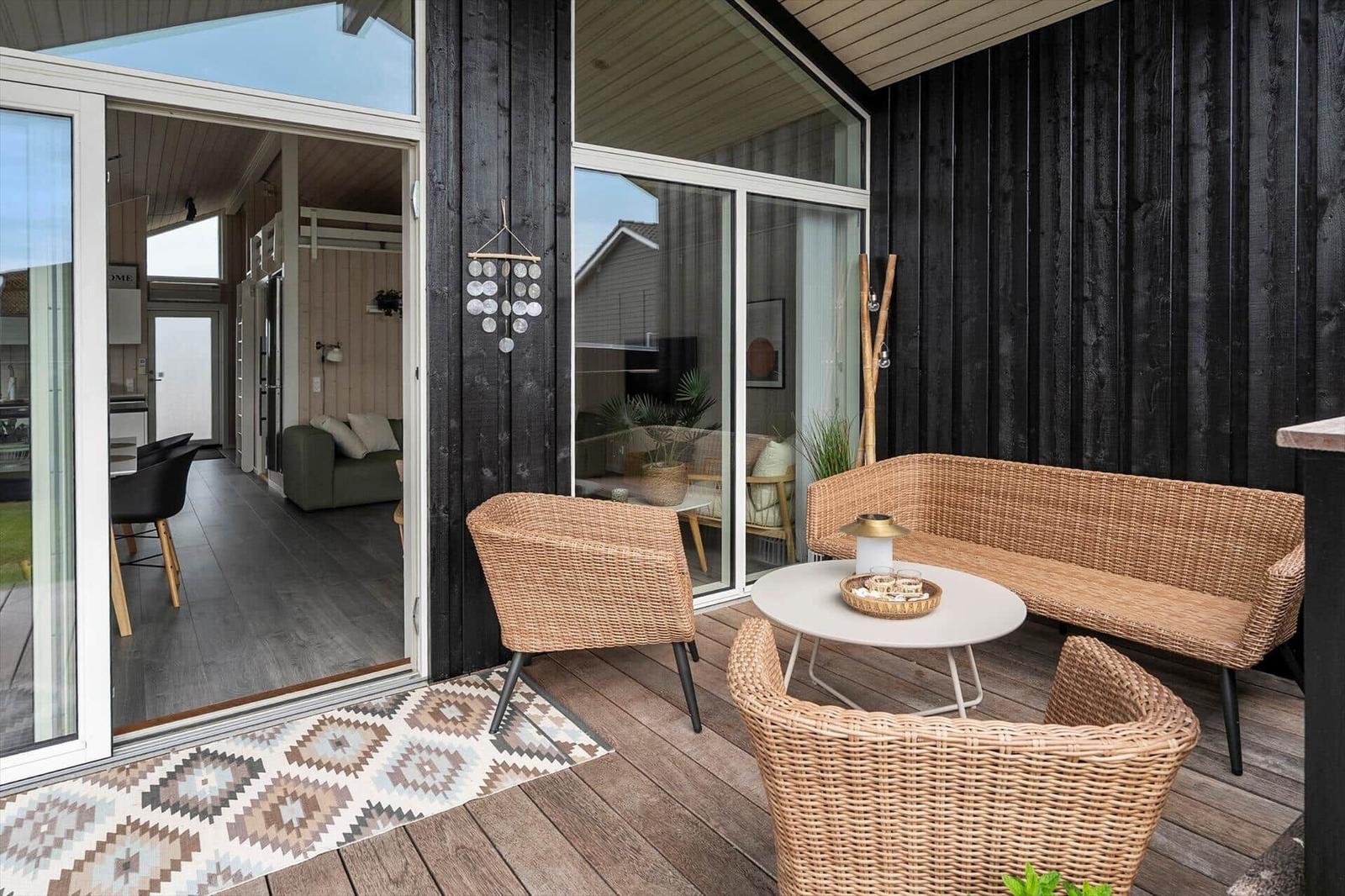 Terrasse mit Tisch und Stühlen, Holzdecke, Pflanzen und Zaun im Hintergrund.
