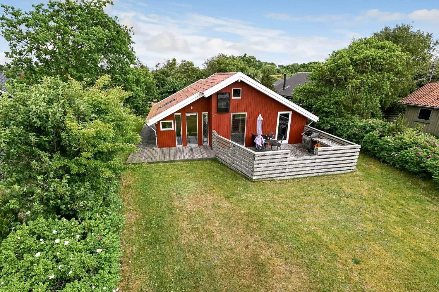 Terrasse mit Grill, Tisch und Sitzbank. Hintergrund: grüne Pflanzen und Haus.