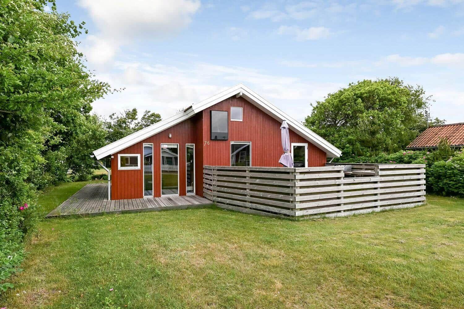 Terrasse mit Tisch, Stühlen, Grill und Bank. Roter Holzwand im Hintergrund.