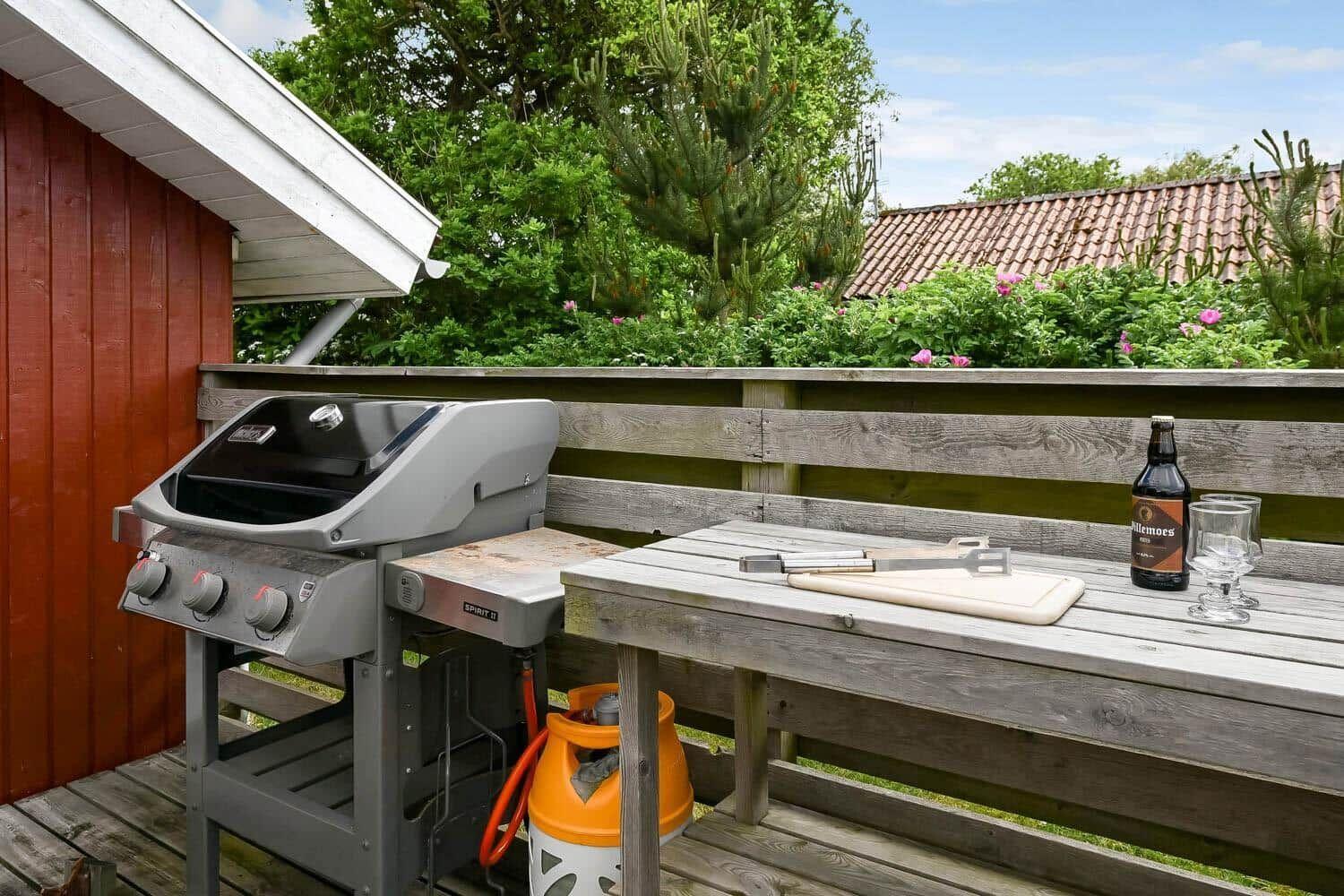 Roter Holzhaus mit Terrasse, Tisch, Stühlen und Grill.