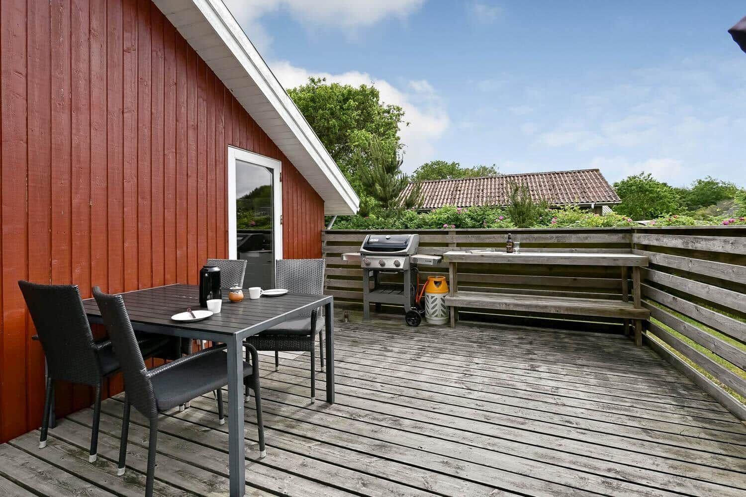 Rotes Haus mit Holzterrasse und Grünfläche unter blauem Himmel.