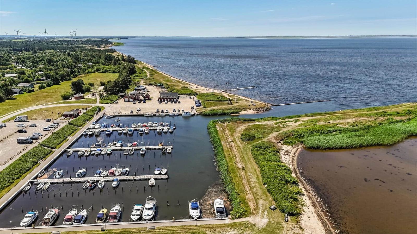 Marina with boats, green areas, and wind turbines in the background.