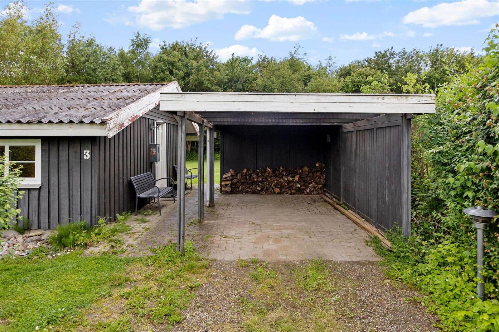 House with woodpile under roof and bench outside.