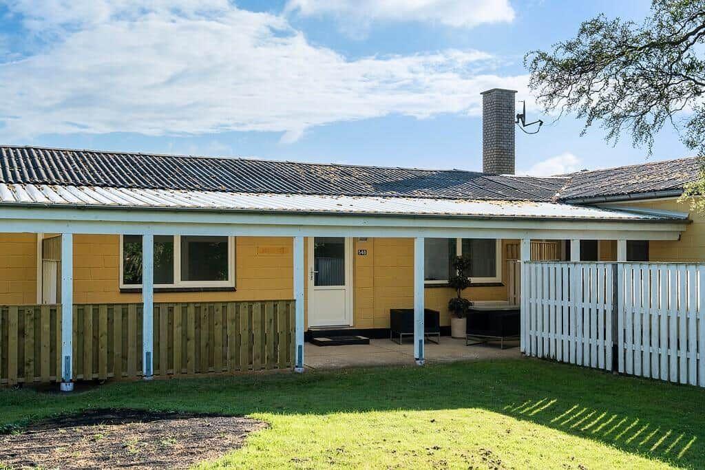 A yellow house with white pillars and a white fence in the front yard.