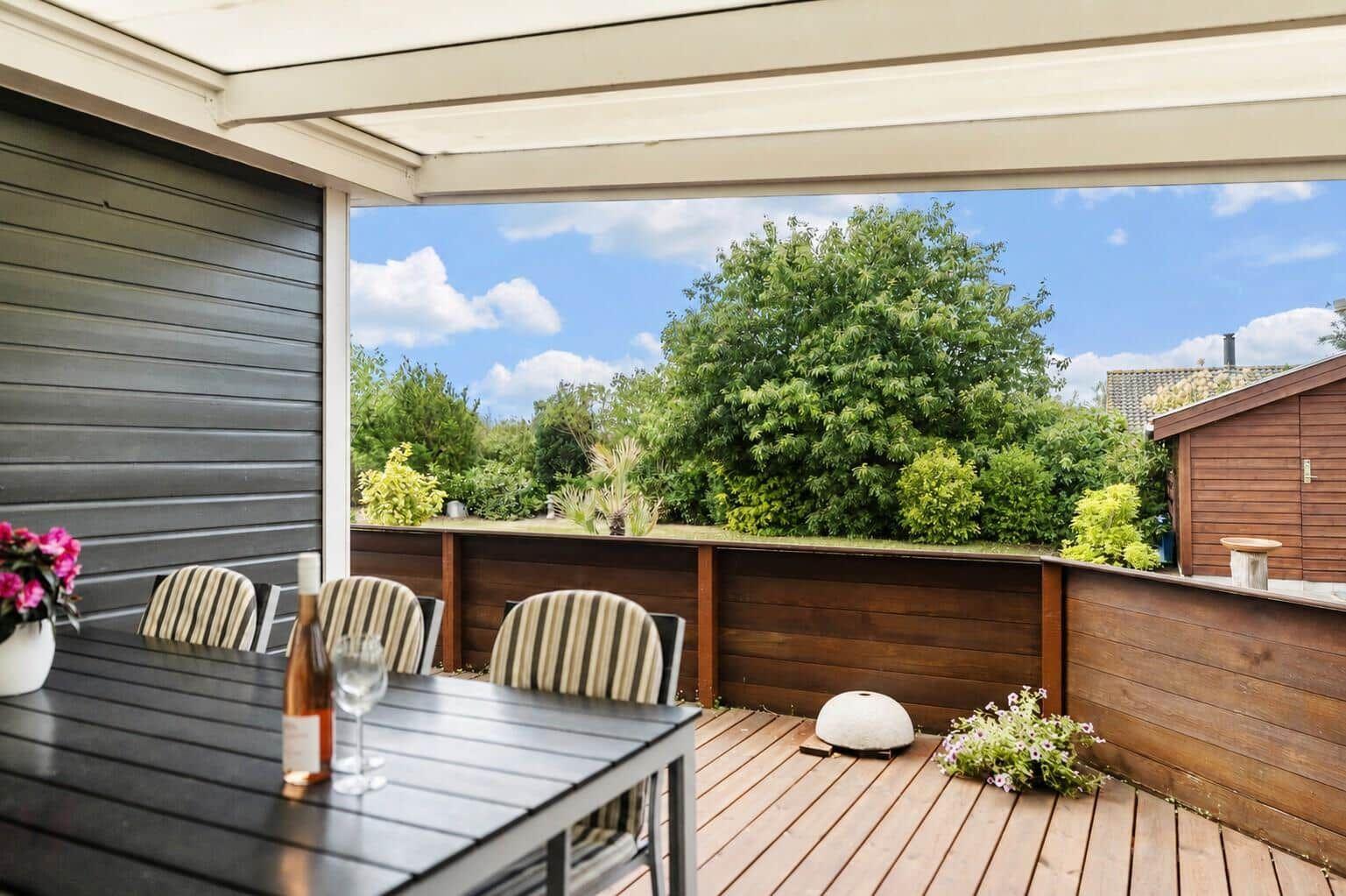 A modern house with terrace, garden, and plants under a blue sky.