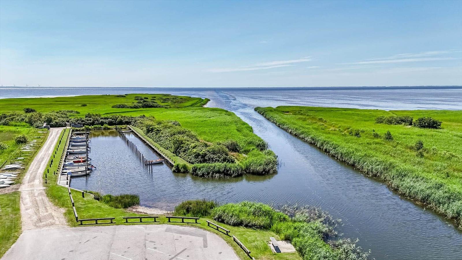 Holzbank auf Kiesfläche mit Blick auf Grasland und Wasser unter blauem Himmel.