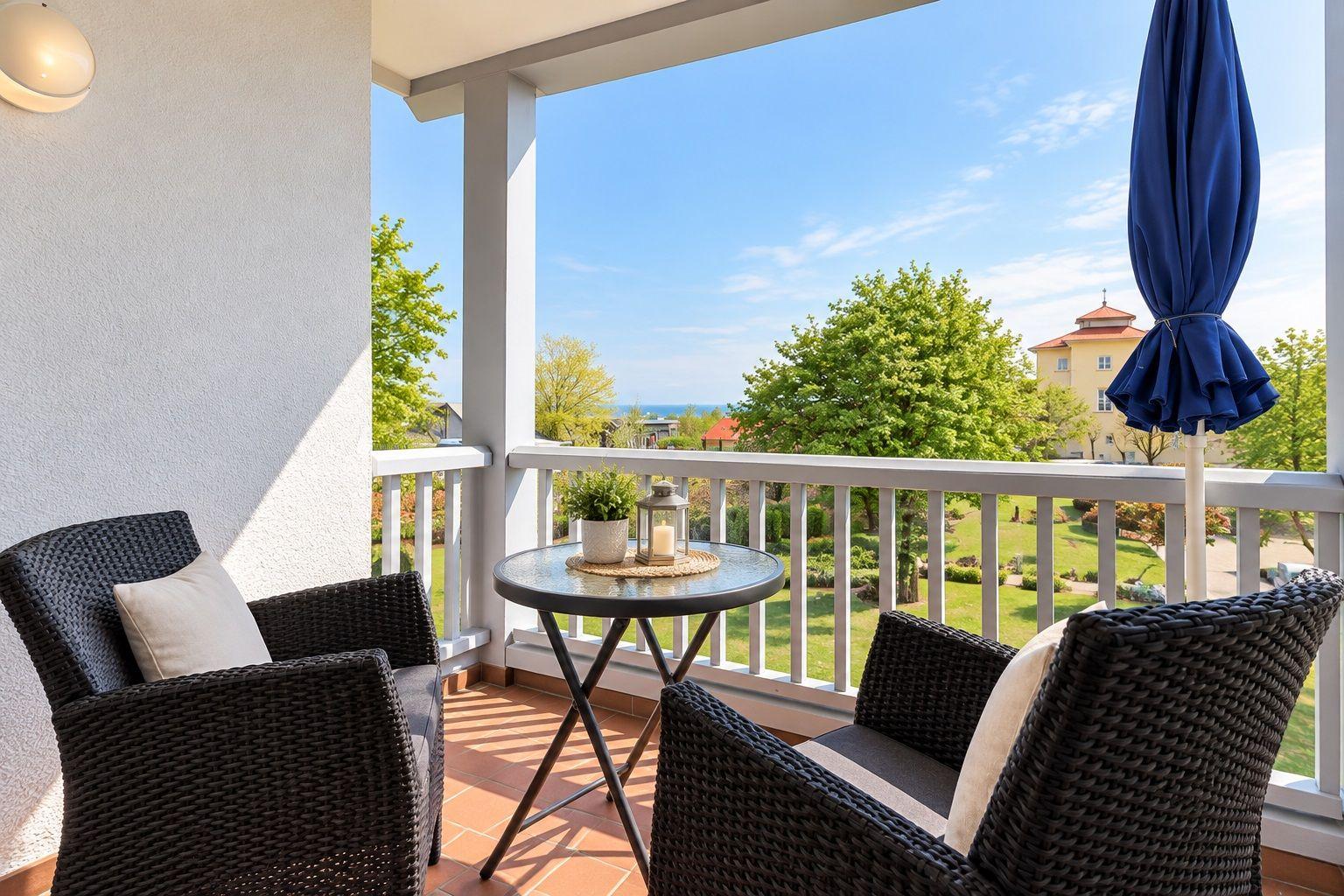 Terrasse mit Tisch, zwei Stühlen und blauem Sonnenschirm. Blick auf Grünfläche und Himmel.