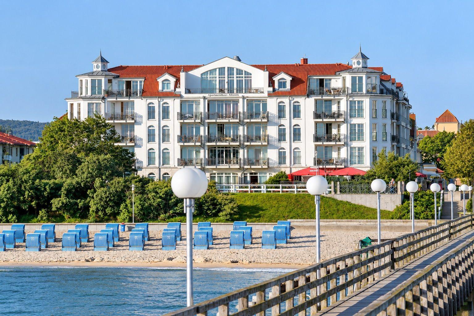 Wohnhaus mit Balkonen und rotem Dach am Strand mit blauen Strandkörben.