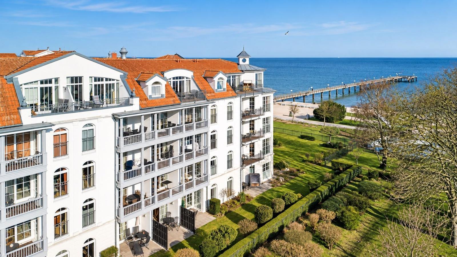 Wohnhaus mit Balkonen und Terrassen, umgeben von Grünanlagen und Blick aufs Meer.