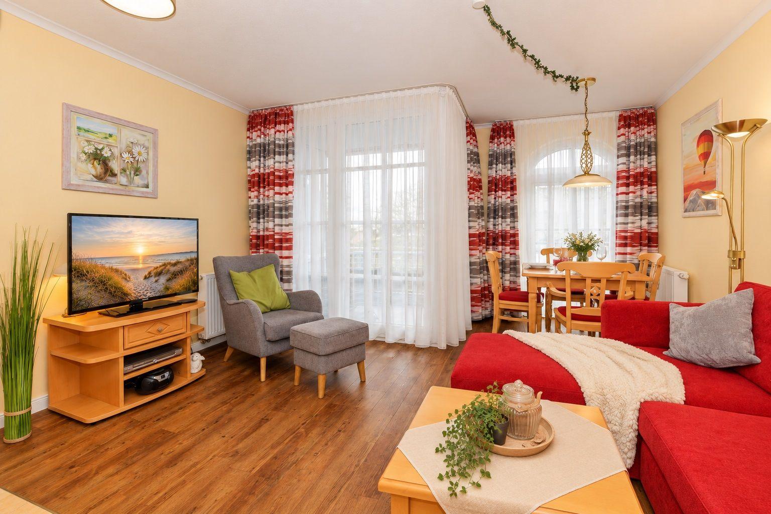 Wohn- und Essbereich mit rotem Sofa, Fernseher und Holztisch.