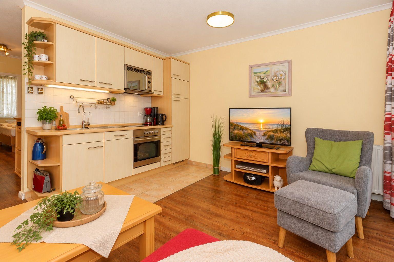 Küche mit Spüle, Herd und Mikrowelle. Wohnbereich mit Sessel, Fernseher und Holzboden.