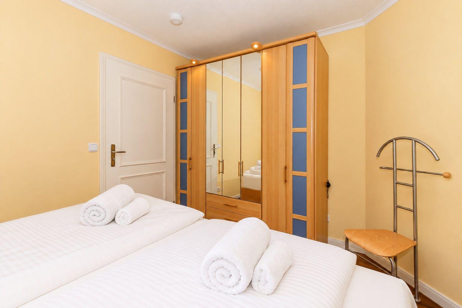 Schlafzimmer mit Bett, Kleiderschrank und Handtuchständer.