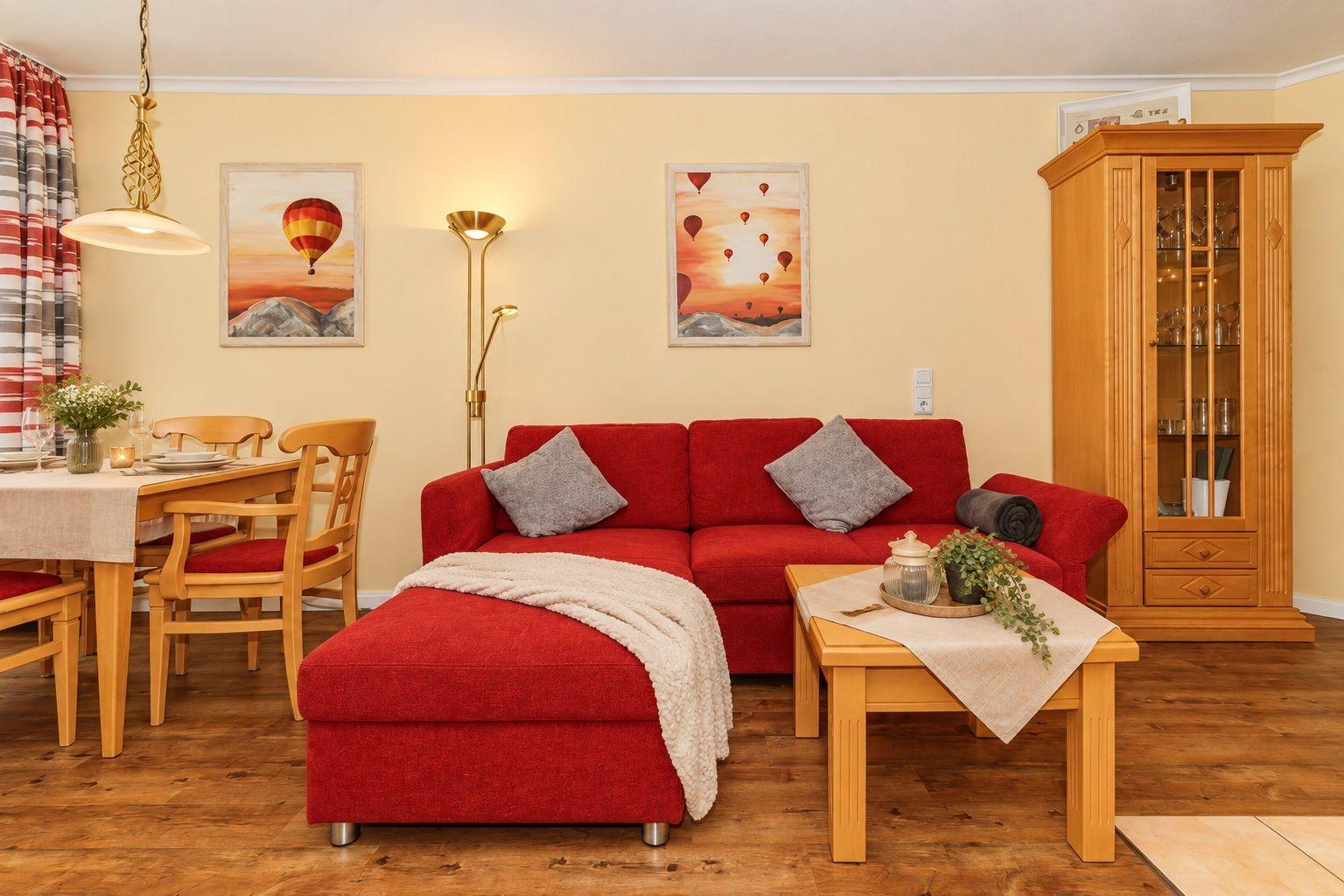 Ein Wohn- und Essbereich mit rotem Sofa, Holzmöbeln und Wandbildern mit Heißluftballons.