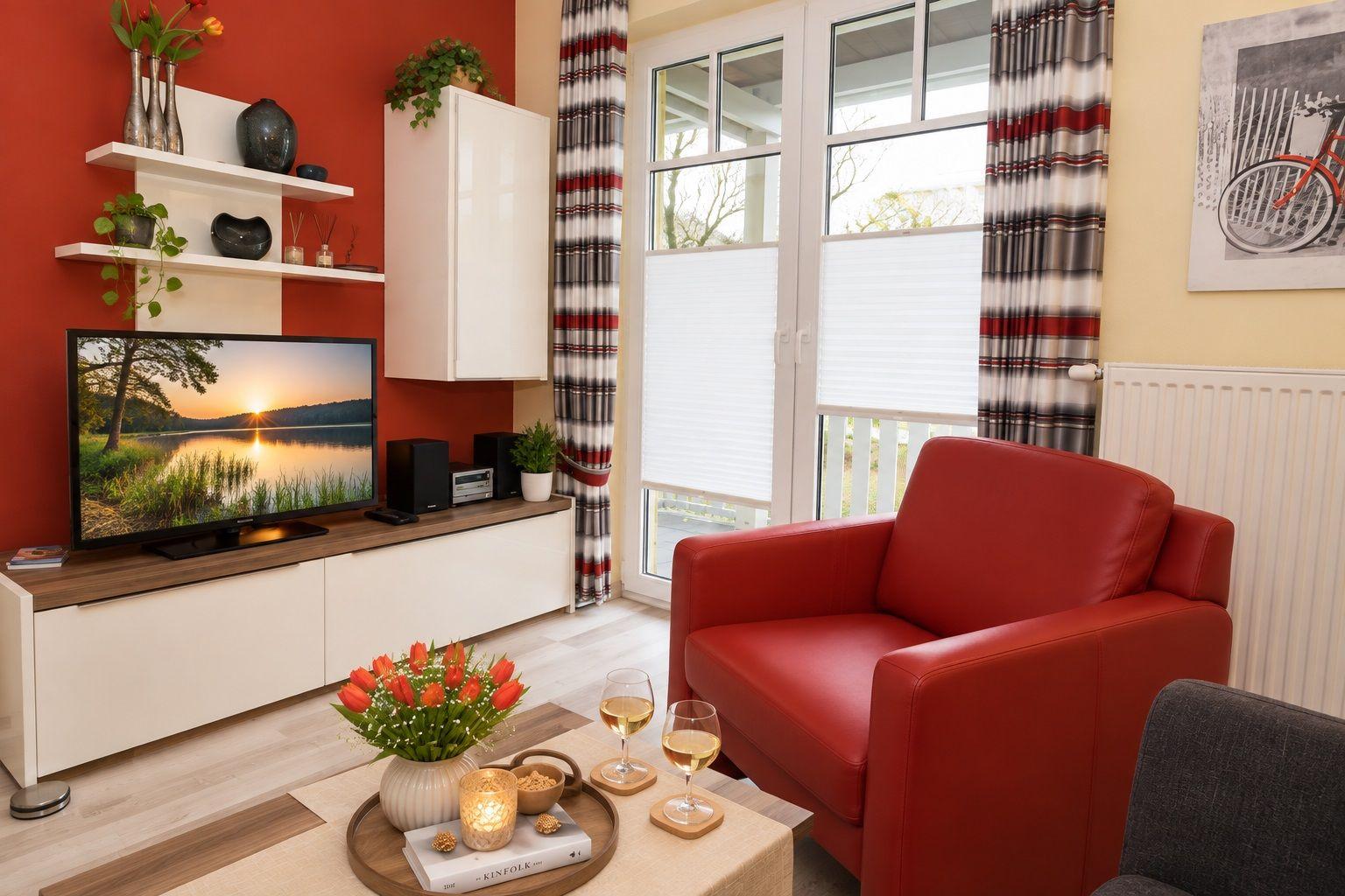 Ein Wohnzimmer mit rotem Sessel, Fernseher und Fenster mit Jalousien.