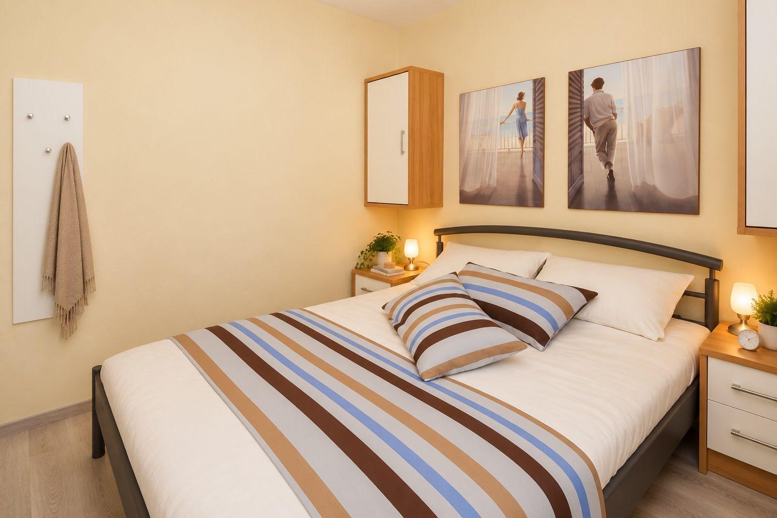 Schlafzimmer mit Bett, Nachttischen und Wandbildern.