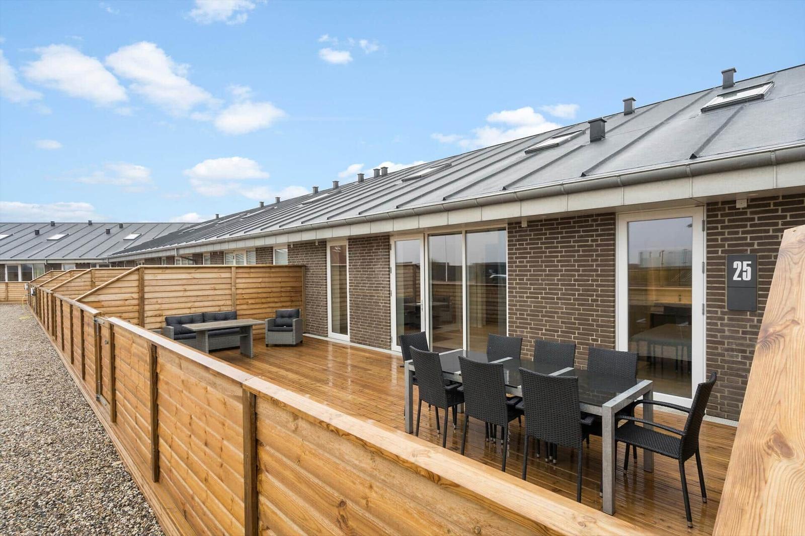 Terrasse mit Holzboden, Gartenmöbeln und Holzumrandung. Hintergrund: Hauswand und blauer Himmel.
