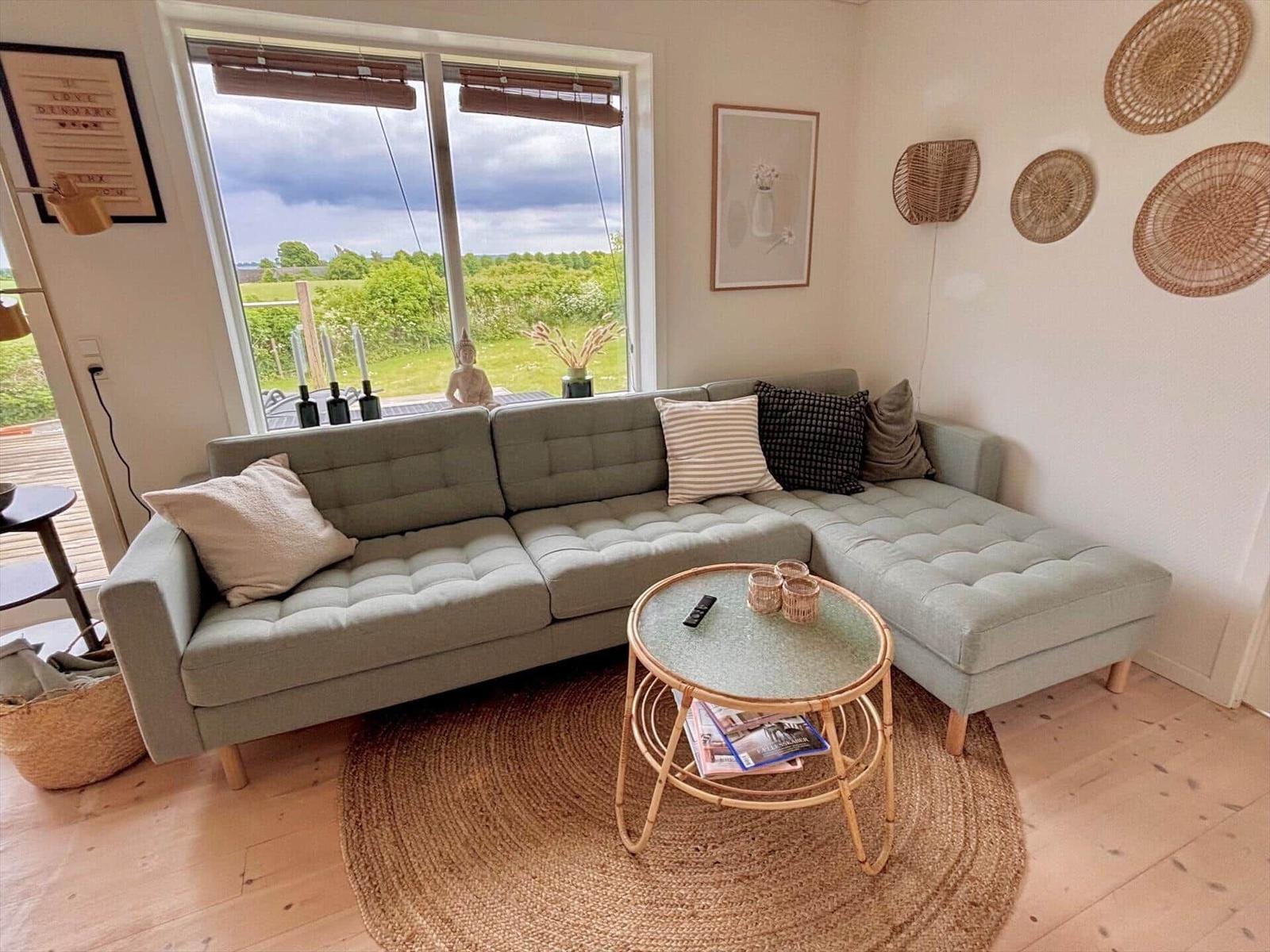Living room with gray sofa, round rug, and round table. Through window you see landscape.