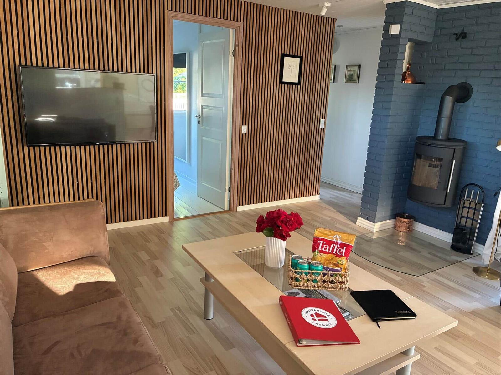 Wohnzimmer mit Fernseher, Holzwand, Kaminofen und Couch.