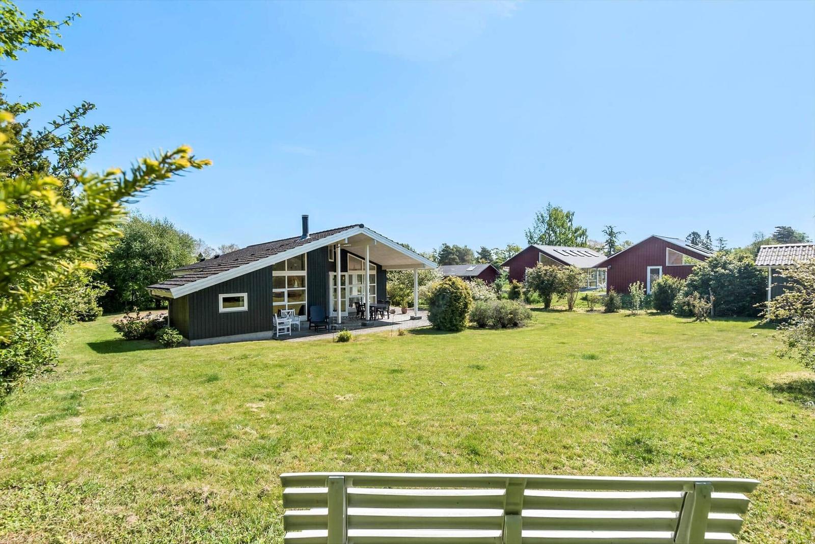 Grüner Garten mit Holzhäusern und einer Bank im Vordergrund.