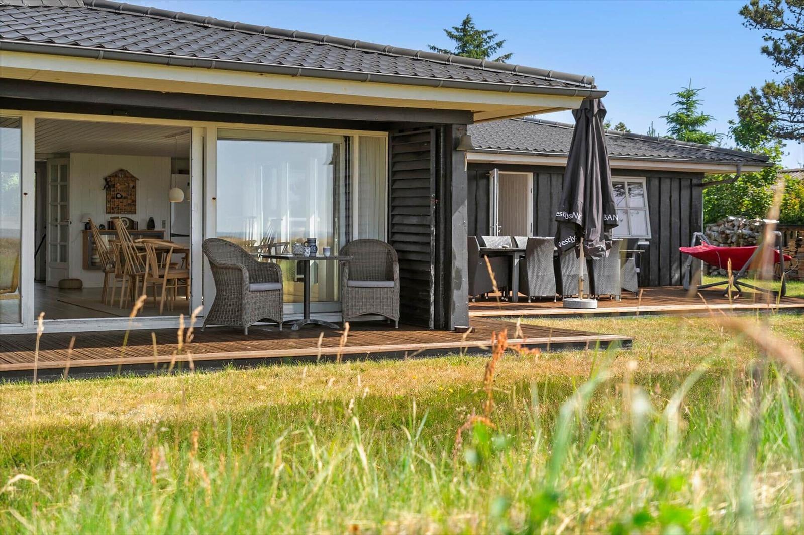 Terrasse mit Liege, Tisch und Stühlen. Blick auf Grasland und Meer.