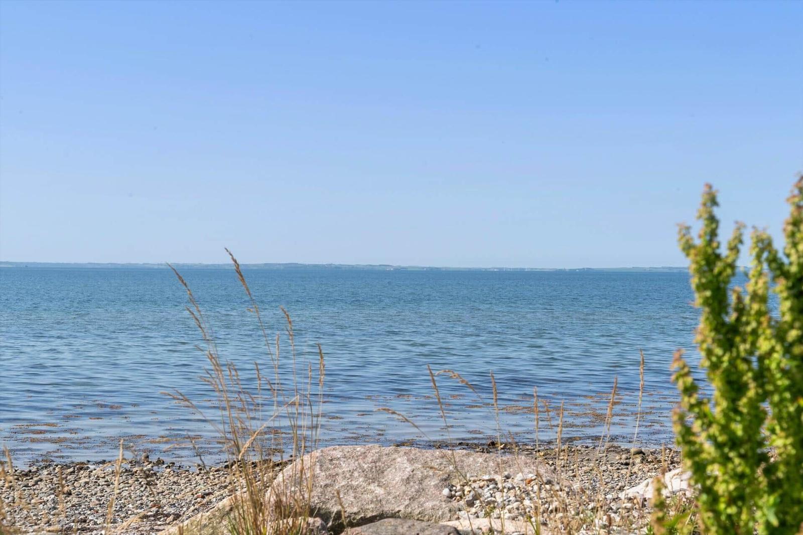 Rundes Holztisch mit Stühlen und Blick auf Grasland und Meer.