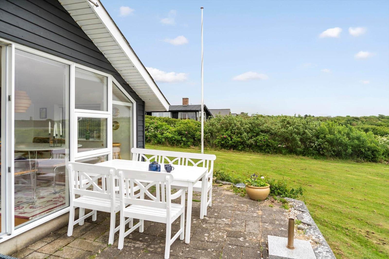 Esszimmer mit Holztisch, schwarzen Stühlen und gelben Wänden. Durchgang zu Terrasse und Wohnbereich.