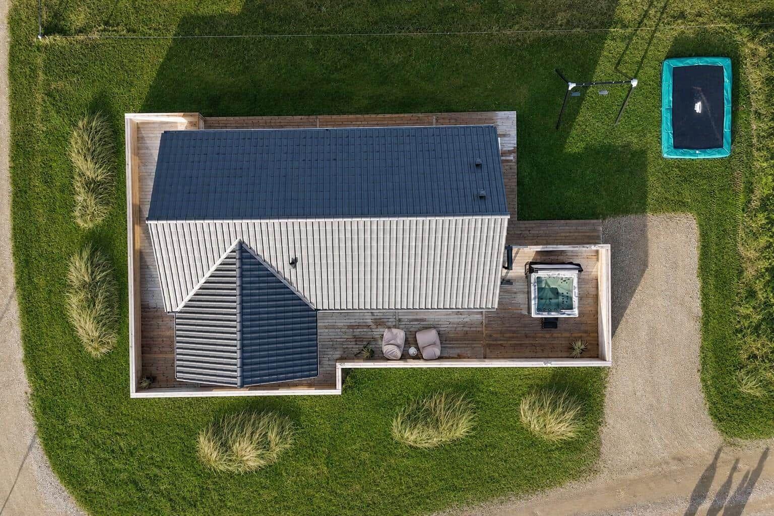 Aerielansicht von Häusern in einer grünen Landschaft mit See und Windkraftanlagen im Hintergrund.