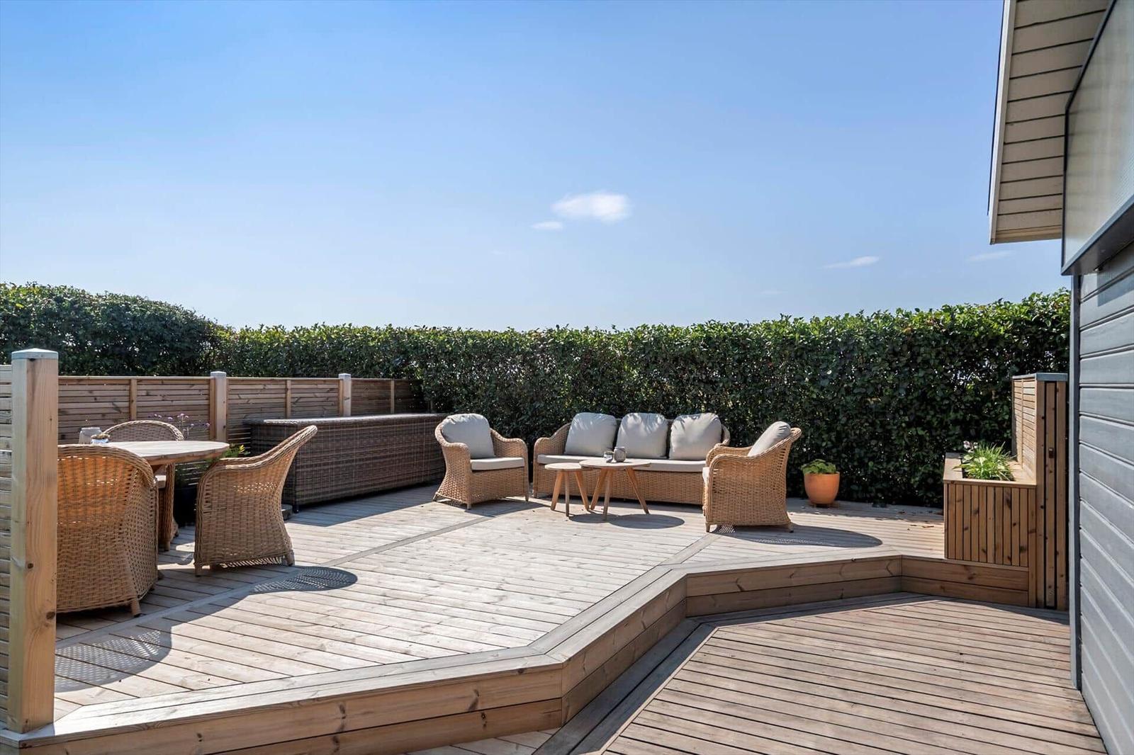 Terrasse mit Sitzgruppe und Tisch, umgeben von Holzgeländer und Hecke.