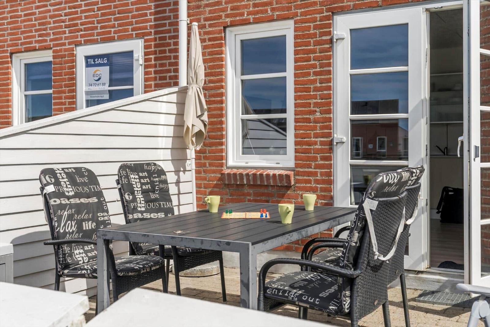 Terrasse mit Tisch und Stühlen, Blick auf Wohnhäuser und Grünfläche.