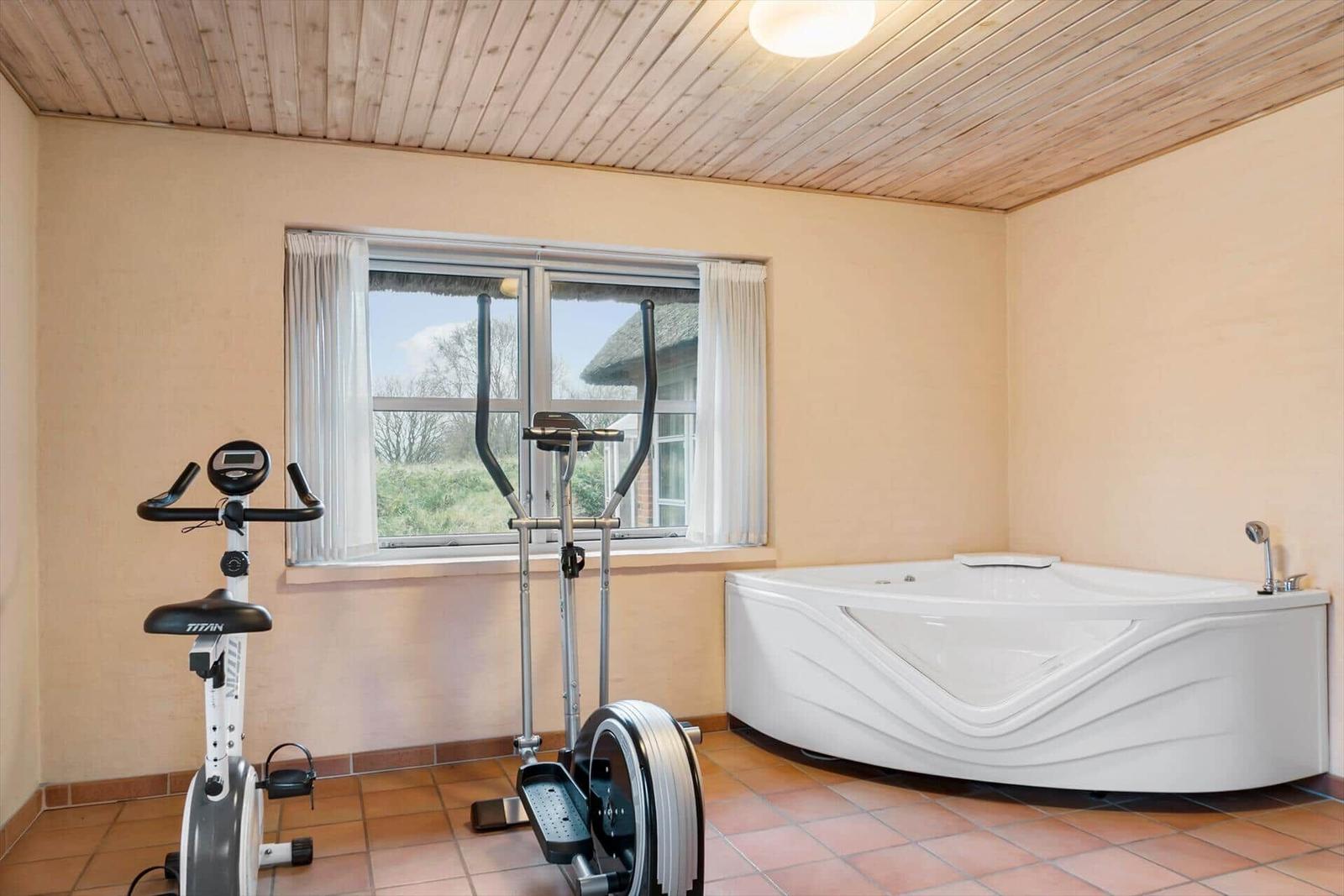 Haus mit Strohdach, Steinmauer und Gartentor. Links steht eine Glasstruktur.