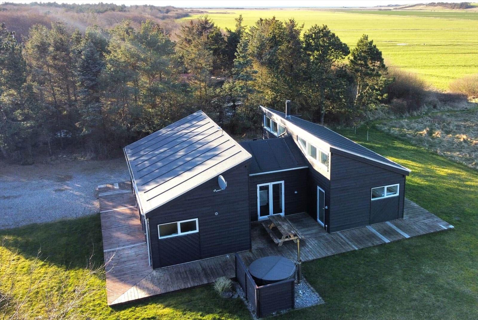 Drei Häuser mit Holzverkleidung und Dach auf grünem Grundstück mit Wald und Meerblick.